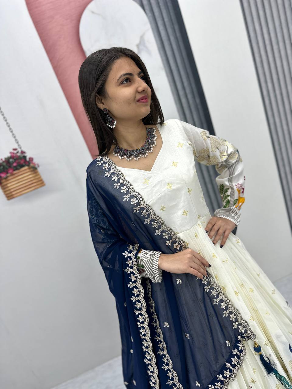 Tarini White Dola Silk Anarkali Gown Set featuring a mesmerizing peacock design with intricate mill print and foil work. Made from premium Dola Silk with a 3-meter flair, it comes with a fully stitched gown and a beautifully embroidered Fox Georgette dupatta adorned with heavy 7mm sequins embroidery. Perfect for festive occasions, weddings, and celebrations, this elegant ensemble blends traditional craftsmanship with contemporary charm